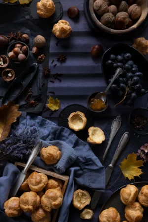 Tło do fotografii kulinarnej i produktowej Autumn Grapes. Kolory głęboki fiolet. Wzór przedstawiający drewniane, fioletowe okiennice. Kadr w stylu dark mood z ciasteczkami z ciasta pażonego, orzechami i winogronem. Listki i kasztany tworzą piękny jesienny kadr.