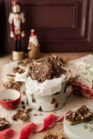 Tło fotograficzne Christmas is Coming które znajduje się w kadrze jako tło tylne. Stylizacja przestawia pudełko słodkości w klimacie świątecznym, Drobne kawałki pokruszone w koło pudełka a dodatkowe elementy w postaci foigurek nadają zdjęciu jeszcze bardziej świątecznewgo klimatu.